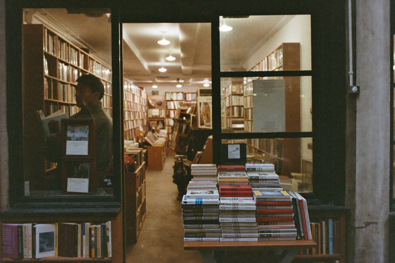 A reader browsing tall wooden shelves in a lamplit bookstore