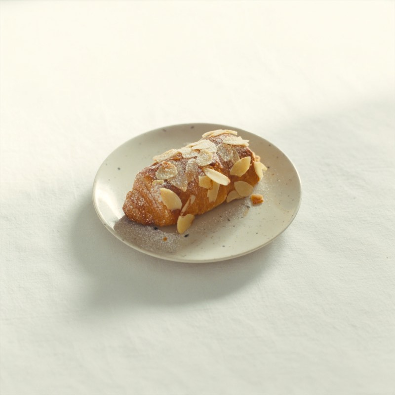 An almond croissant dusted with icing sugar on a ceramic plate