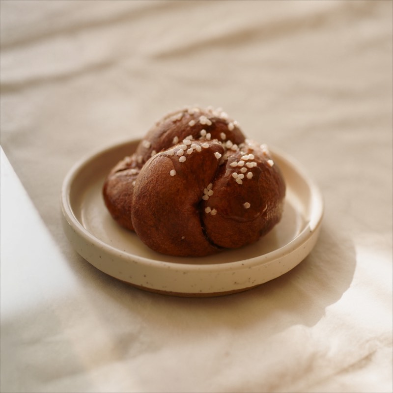 A knotted cardamom bun topped with pearl sugar on a ceramic plate
